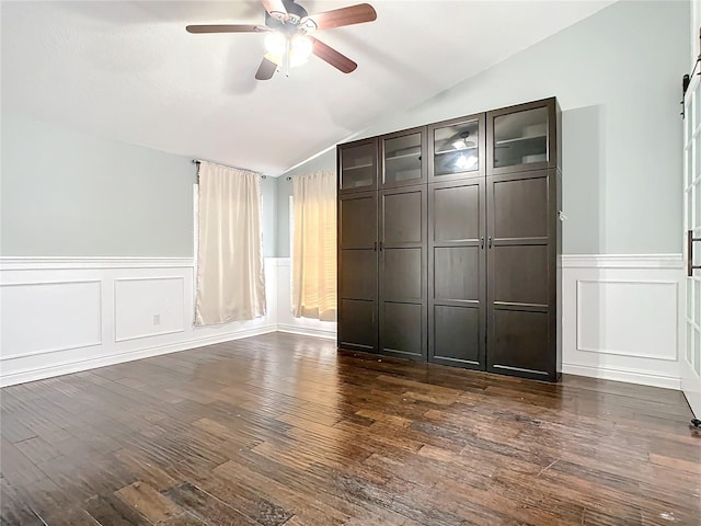 interior space featuring a barn door, ceiling fan, dark wood-type flooring, and vaulted ceiling