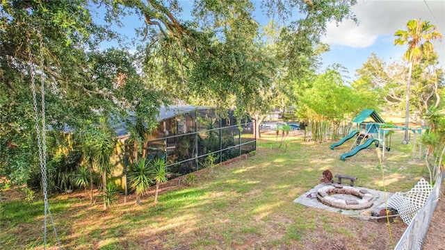 view of yard with a playground, glass enclosure, and a fire pit