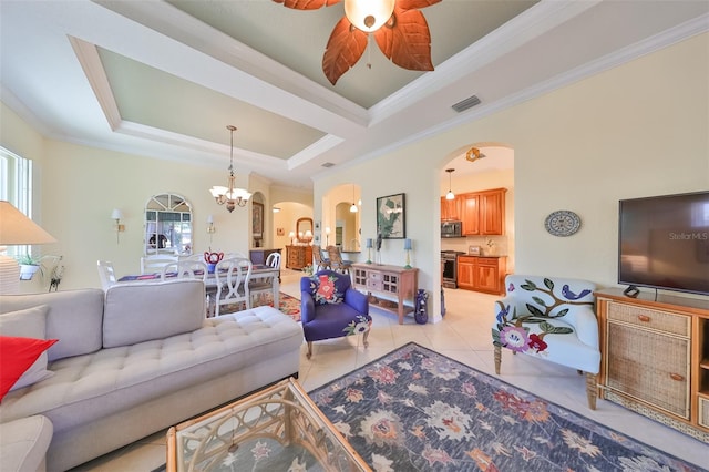 tiled living room featuring a tray ceiling, ornamental molding, and ceiling fan with notable chandelier