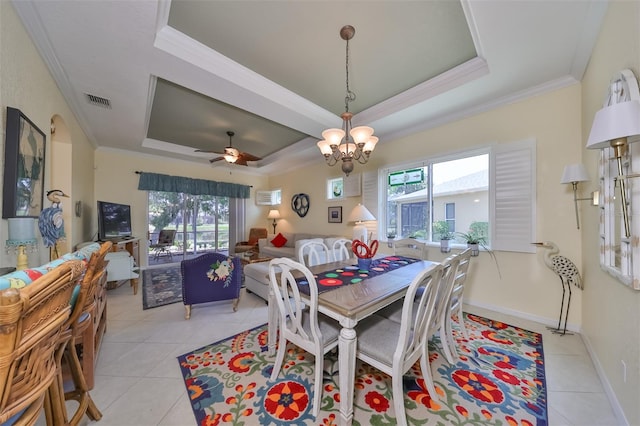 tiled dining area featuring ornamental molding, ceiling fan with notable chandelier, and a raised ceiling