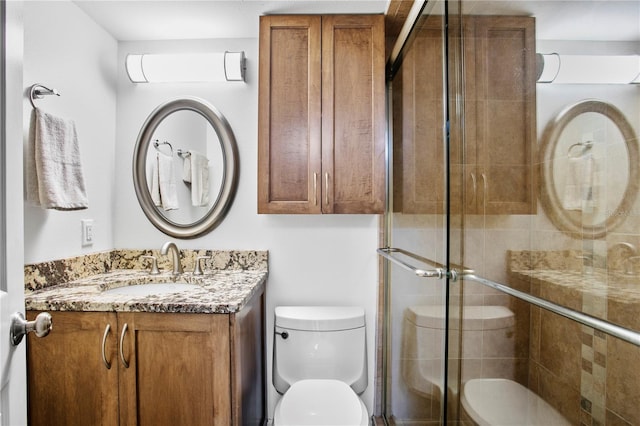 bathroom with a shower with shower door, vanity, and toilet