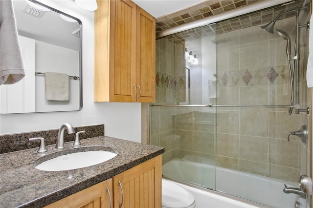 full bathroom with combined bath / shower with glass door, vanity, and toilet