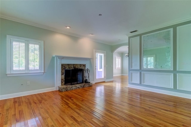 unfurnished living room with crown molding, a stone fireplace, and light wood-type flooring