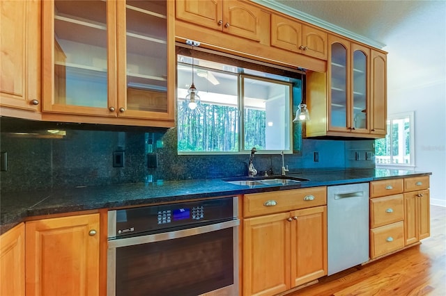 kitchen with dark stone countertops, sink, light wood-type flooring, appliances with stainless steel finishes, and tasteful backsplash