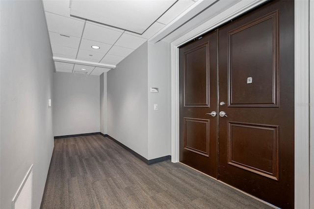 hallway featuring a drop ceiling and dark colored carpet