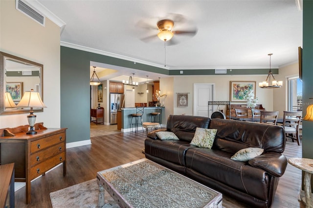 living room with ceiling fan with notable chandelier, dark wood-type flooring, and crown molding