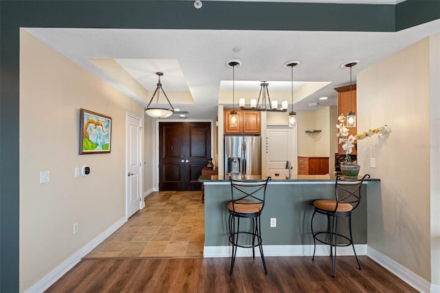 kitchen with kitchen peninsula, pendant lighting, a raised ceiling, and stainless steel refrigerator with ice dispenser