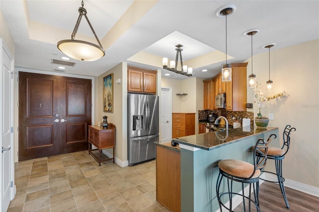 kitchen with backsplash, appliances with stainless steel finishes, hanging light fixtures, and a raised ceiling