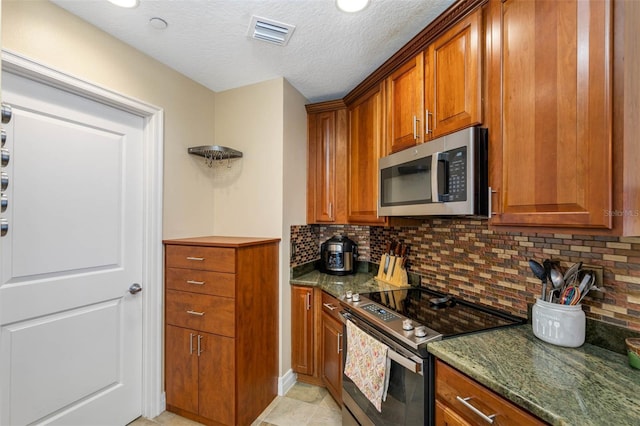 kitchen with light tile floors, a textured ceiling, tasteful backsplash, dark stone counters, and stainless steel appliances