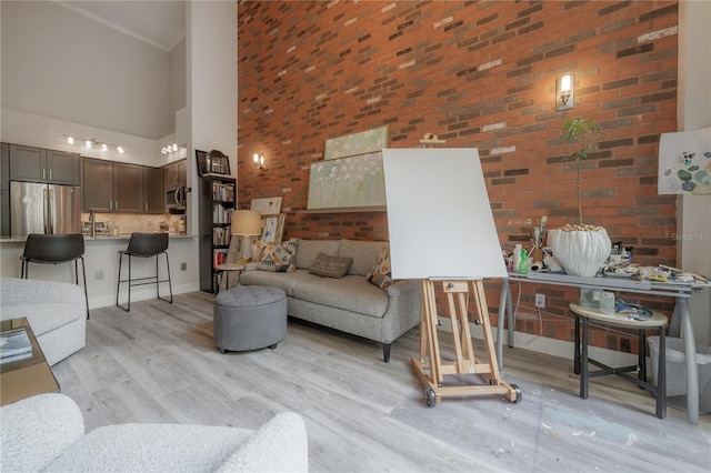 living room featuring brick wall, a high ceiling, and light wood-type flooring