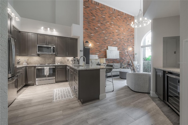 kitchen featuring brick wall, appliances with stainless steel finishes, high vaulted ceiling, and light wood-type flooring