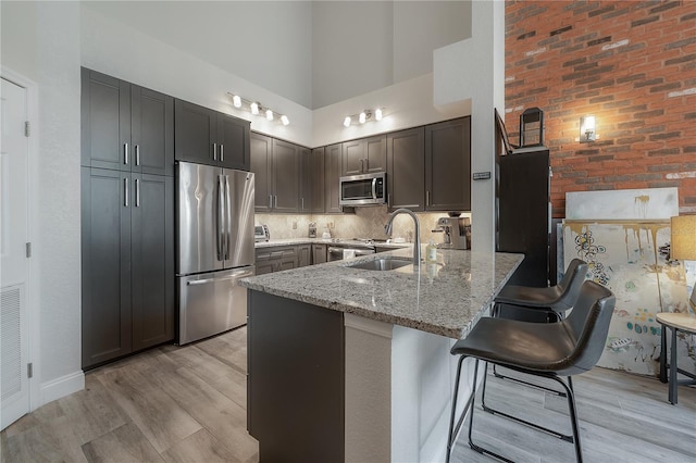 kitchen with light stone countertops, light hardwood / wood-style flooring, a high ceiling, brick wall, and appliances with stainless steel finishes