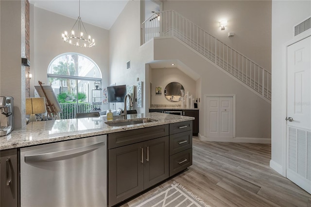 kitchen with light stone countertops, light wood-type flooring, a high ceiling, sink, and dishwasher