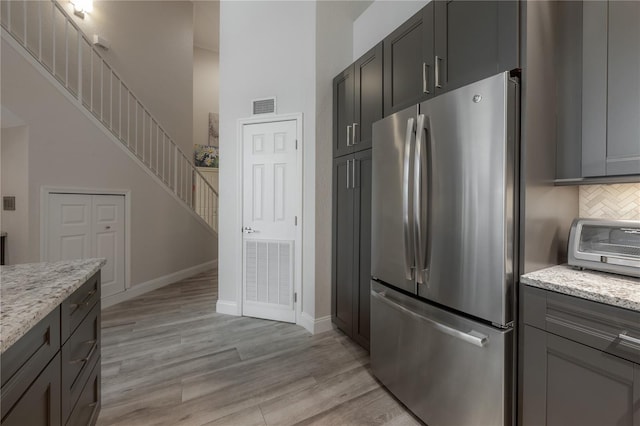 kitchen featuring light stone counters, backsplash, stainless steel fridge, and light wood-type flooring