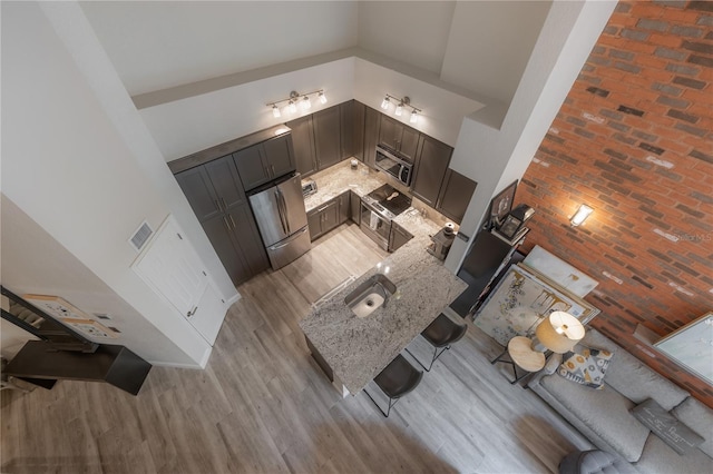 unfurnished living room with high vaulted ceiling, sink, brick wall, and light wood-type flooring