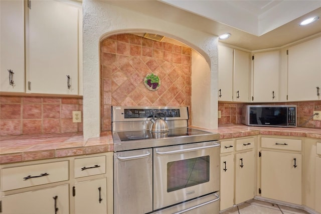 kitchen with decorative backsplash, light tile patterned floors, cream cabinetry, tile counters, and stainless steel appliances