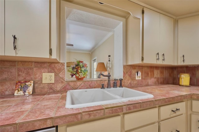 kitchen with cream cabinetry, ornamental molding, sink, and tile countertops