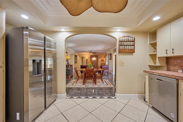 kitchen with crown molding, light tile patterned floors, a tray ceiling, white cabinetry, and stainless steel appliances