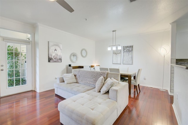 living room with ceiling fan with notable chandelier, ornamental molding, and dark wood-type flooring