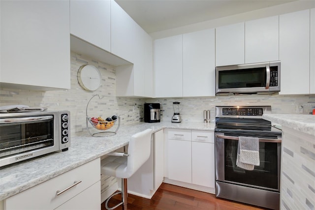 kitchen with stainless steel appliances, dark wood-type flooring, white cabinets, and backsplash