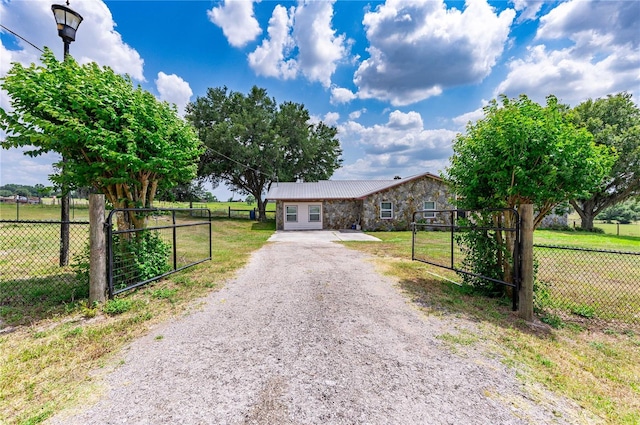 single story home featuring gravel driveway, stone siding, fence, and a front lawn