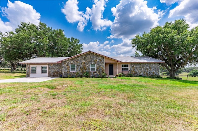 view of front of property featuring driveway, stone siding, metal roof, and a front yard