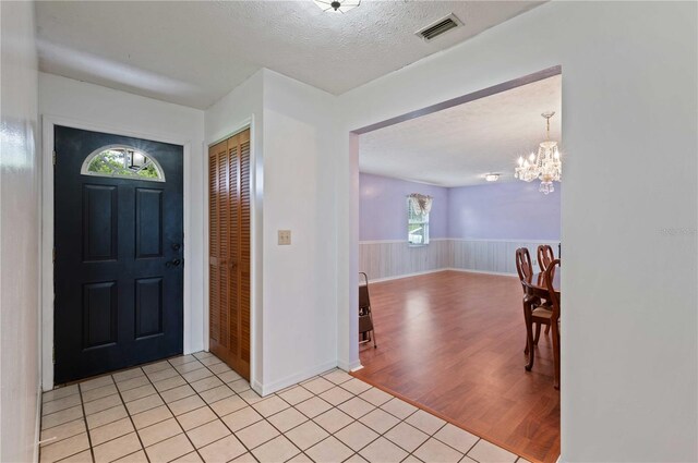 foyer entrance with wainscoting, visible vents, a textured ceiling, and light tile patterned floors