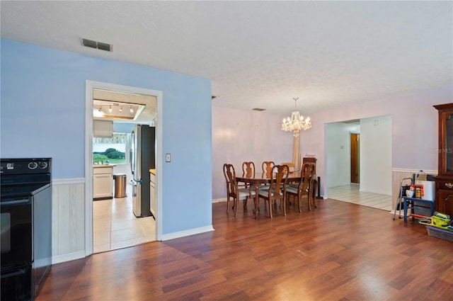 dining space featuring a textured ceiling, wood finished floors, visible vents, and an inviting chandelier