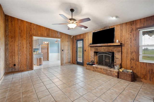 unfurnished living room with ceiling fan, wood walls, a brick fireplace, and light tile patterned flooring