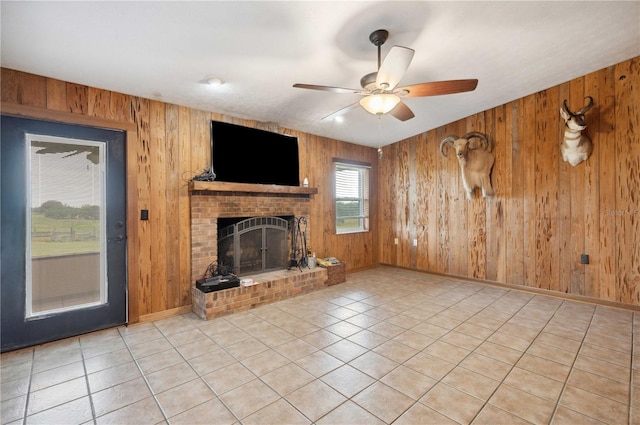 unfurnished living room featuring ceiling fan, light tile patterned floors, wood walls, and a brick fireplace