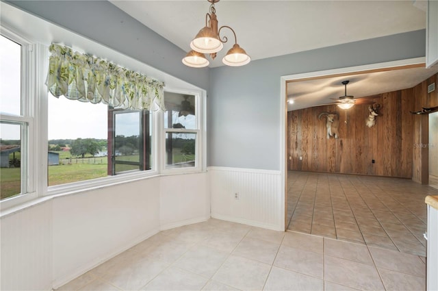 unfurnished dining area featuring ceiling fan, light tile patterned floors, a healthy amount of sunlight, and wooden walls