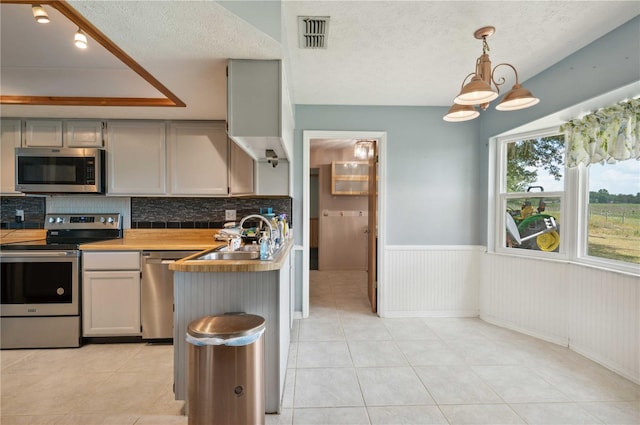 kitchen featuring gray cabinetry, stainless steel appliances, butcher block counters, and pendant lighting