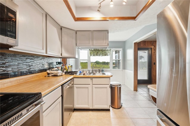 kitchen with light tile patterned floors, appliances with stainless steel finishes, backsplash, a tray ceiling, and sink