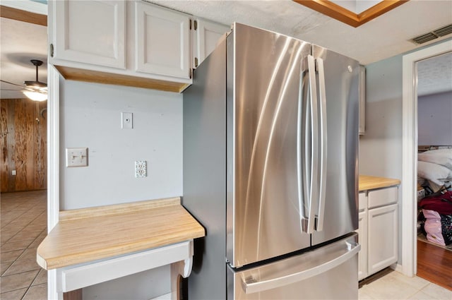 kitchen featuring light tile patterned flooring, ceiling fan, white cabinetry, and stainless steel refrigerator