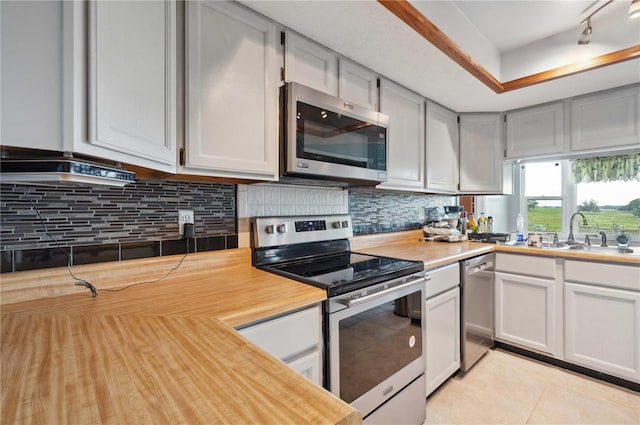 kitchen featuring light tile patterned floors, a sink, appliances with stainless steel finishes, decorative backsplash, and a raised ceiling