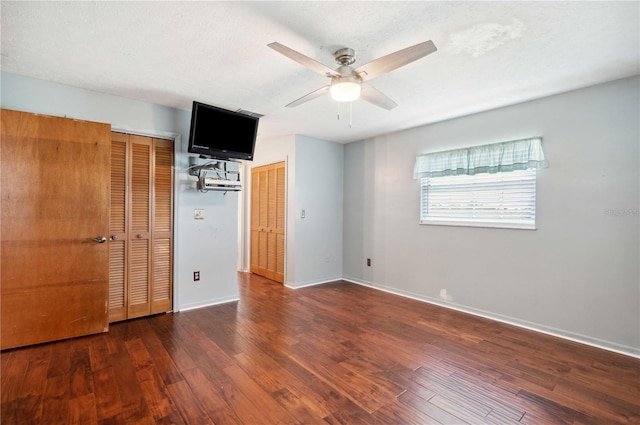 unfurnished bedroom featuring ceiling fan, dark wood-type flooring, a textured ceiling, and two closets