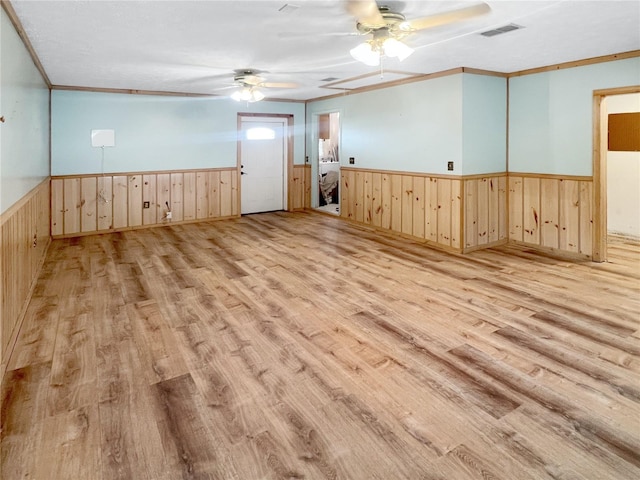 empty room with wainscoting, crown molding, visible vents, and light wood finished floors