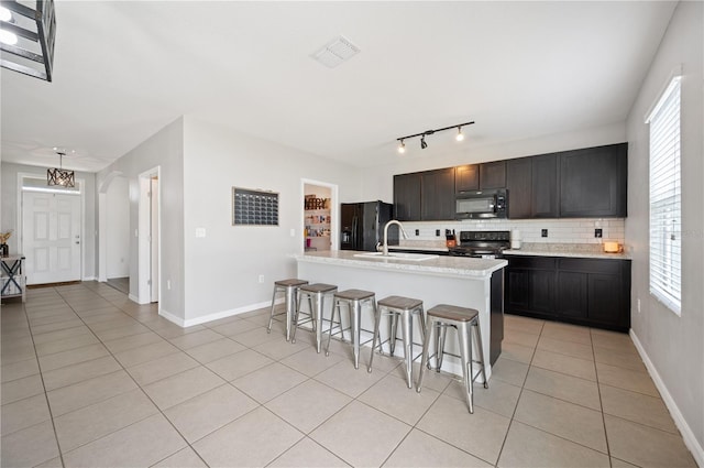 kitchen with a healthy amount of sunlight, black appliances, a breakfast bar area, light tile floors, and an island with sink