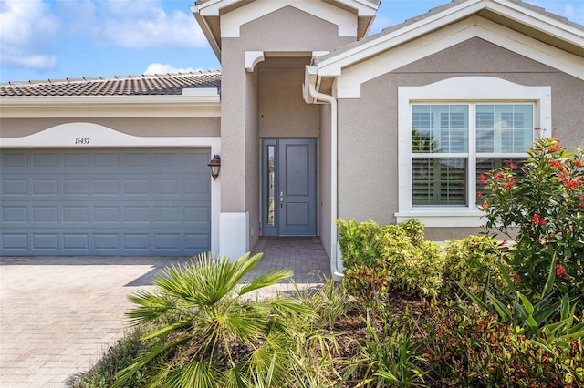 entrance to property featuring stucco siding, decorative driveway, a garage, and a tiled roof