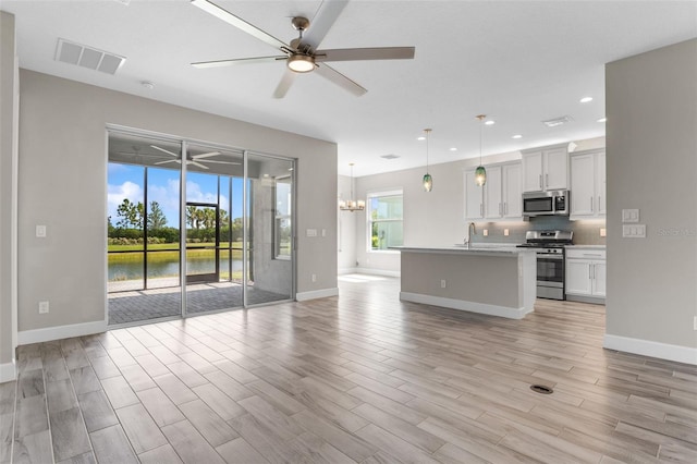 unfurnished living room featuring ceiling fan with notable chandelier, a water view, and sink