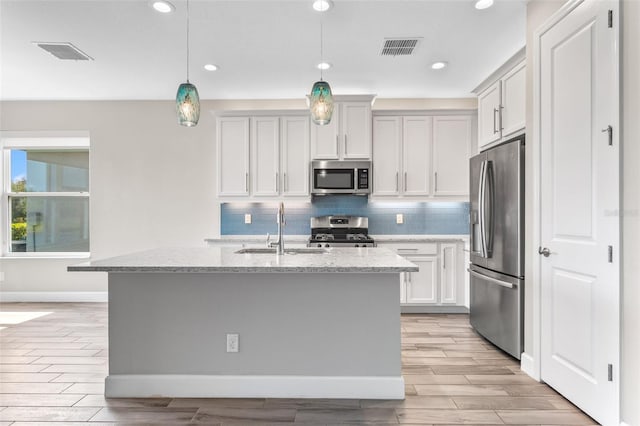 kitchen with stainless steel appliances, a kitchen island with sink, hanging light fixtures, and sink