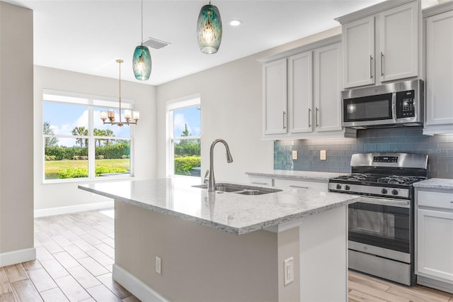 kitchen with light stone countertops, appliances with stainless steel finishes, a kitchen island with sink, and sink