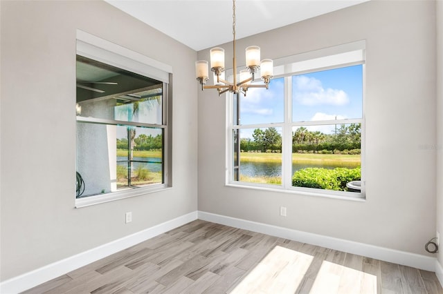 unfurnished dining area with a water view, a chandelier, and light hardwood / wood-style floors