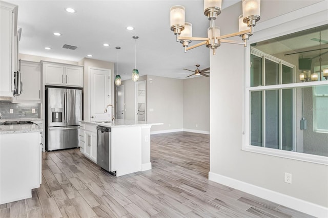 kitchen with appliances with stainless steel finishes, backsplash, ceiling fan with notable chandelier, a kitchen island with sink, and pendant lighting