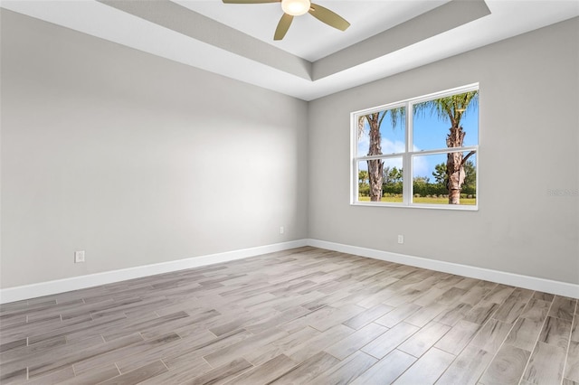 spare room with a raised ceiling, ceiling fan, and light hardwood / wood-style floors