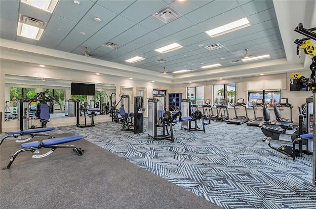 gym with a tray ceiling, ceiling fan, a drop ceiling, and carpet