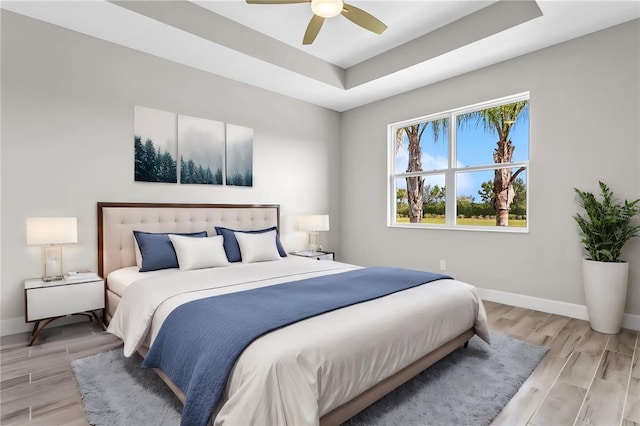 bedroom featuring ceiling fan, light hardwood / wood-style flooring, and a tray ceiling