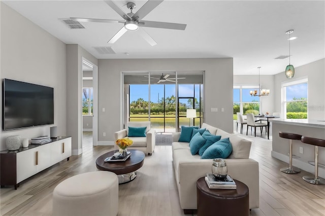 living room with ceiling fan with notable chandelier and light hardwood / wood-style flooring