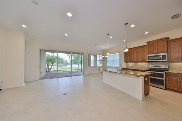 kitchen with appliances with stainless steel finishes, pendant lighting, decorative backsplash, light stone counters, and a center island with sink