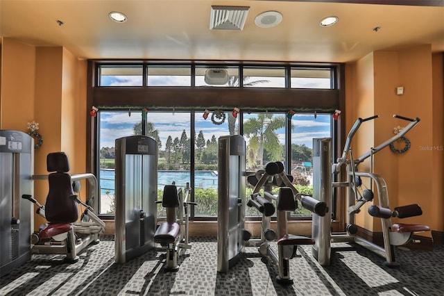 exercise room with dark colored carpet and a water view